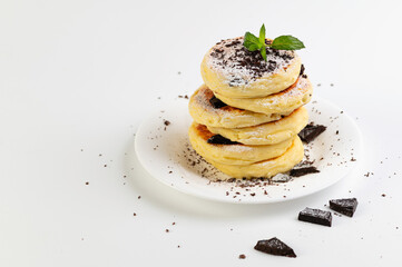 cottage cheese pancakes, curds on a white dessert plate with chocolate and mint on a white background, place for text