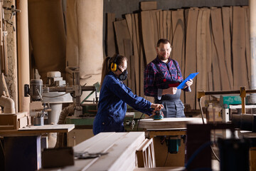 Young female apprentice polishing wood under senior colleague supervision
