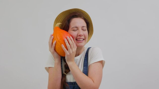 Farmer woman in overalls and a hat clutches a ripe orange pumpkin. Concept of vegetarianism and agriculture.