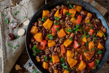 Stew with pumpkin, ground beef, kidney beans and vegetable in rustic cast iron skillet. Delicious meal for autumn and winter season