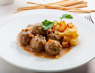 Albóndigas caseras con salsa y patatas fritas cortada en cuadrados. Homemade meatballs with sauce and French fries cut into squares.