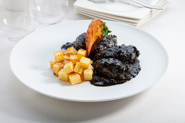 Calamares en su tinta con patatas fritas en plato blanco. Squid in its ink with French fries on a...