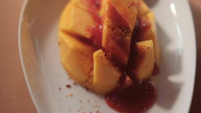 Plate of chopped mango with Mexican chamoy sauce and blurry background