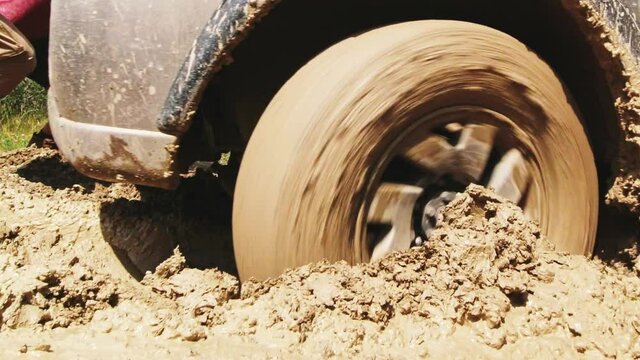 Close up view 4WD vehicle front wheel stuck in mud go backwards pushed by two men outdoors in nature. Extreme road conditions summer after rain concept