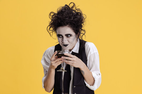 Portrait of woman with messy hair and creepy makeup having viperous facial expression isolated on yellow background. Halloween party
