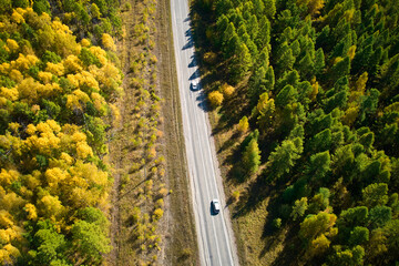 Road through autumn forest from the air. Beautiful asphalt roadway to lake Baikal on a sunny autumn day, in Siberia.
