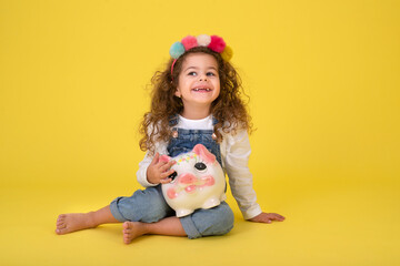 Happy  Little Children girl  saved a little money for future need wearing white T-shirt holding piggy bank, Saving money since childhood on yellow background  studio shot with copy space