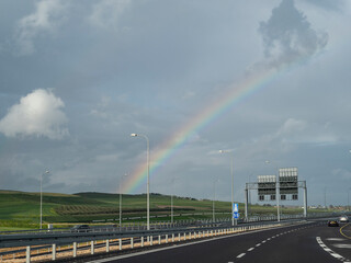 Rainbow in the cloudy sky and the highway stretching into the distance.