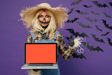 Young woman with Halloween mask in straw hat scarecrow costume hold use work on laptop pc computer...