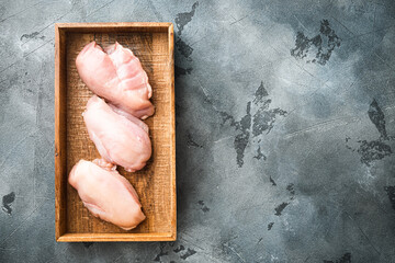 Raw organic chicken Breasts, in wooden box, on gray stone background, top view flat lay, with copy space for text