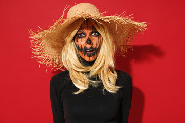Young displeased disappointed dissatisfied woman with Halloween makeup mask wears straw hat black scarecrow costume isolated on plain red background studio portrait. Celebration holiday party concept.