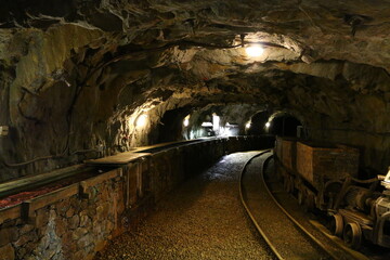 Antique and rusted interior of an old copper mine including dark tunnels, tungsten light, railroad track, rusty wagons, broken wheels and other mining equipment