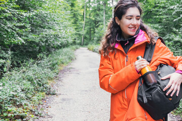 A woman picking up a metal bottle from her backpack. Adventure concept. Trekking concept. Copy space