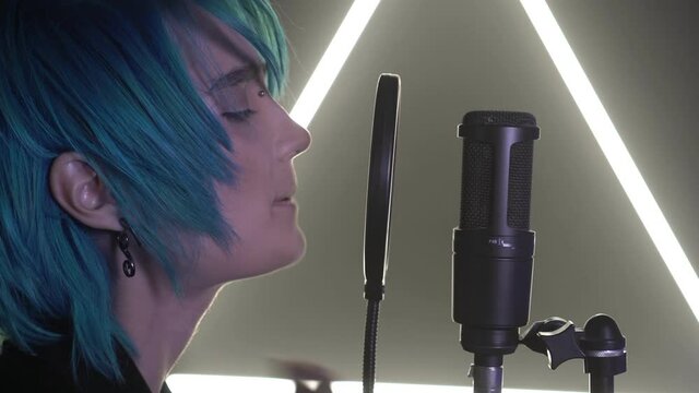 Handsome man or woman with blue hair sings into a microphone, close-up