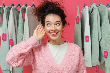 Young fun female costumer woman 20s wear sweater stand near clothes rack with tag sale in store...