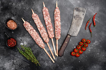Raw mutton kebab shish skewers, with grill ingredients, on black dark stone table background, top...