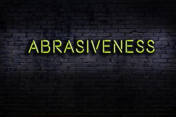 Neon sign. Word abrasiveness against brick wall. Night view
