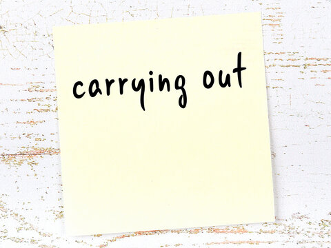 Yellow sheet of paper with word carrying out. Reminder concept