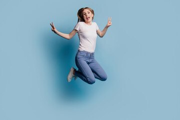 Photo of crazy excited funny dream lady jump show v-sign wear jeans casual clothes on blue color background
