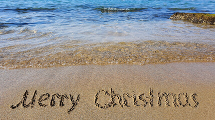 Fototapeta premium Word Merry Christmas written on the sand near the sea.