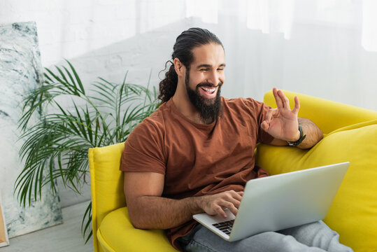 cheerful latin man showing okay gesture while using laptop on sofa at home