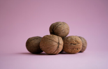 Whole dark walnut in a shell on a light pink background