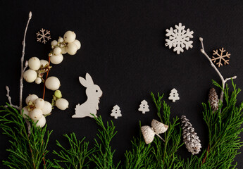 Stylish christmas composition on a black background, wooden figurines of hare, snowflakes and fir branches, copy space