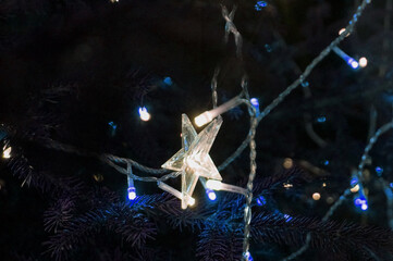 White lights on the Christmas tree. Star shaped decoration. Bright Christmas Eve in dark night.