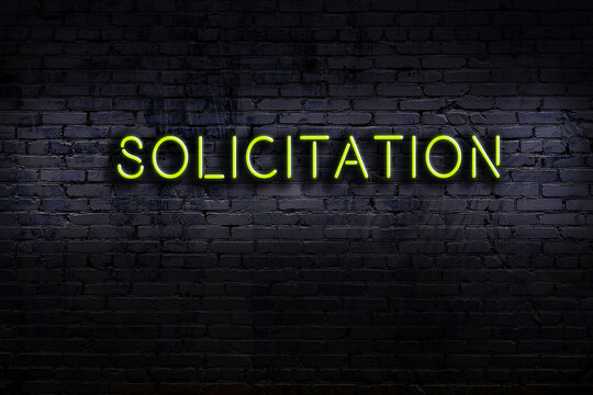 Night view of neon sign on brick wall with inscription solicitation