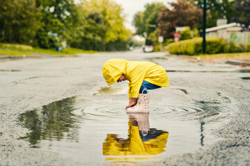 Funny cute baby girl wearing yellow waterproof coat and boots playing in the rain