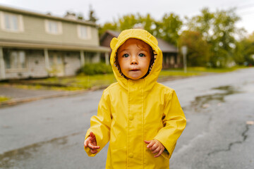 Funny cute baby girl wearing yellow waterproof coat and boots playing in the rain