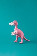 Pink painted dinosaur toy holding gifts for Christmas or New Year. Minimal winter holidays idea on green blue background. Creative composition.