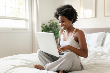 young black woman using a laptop in bright bedroom
