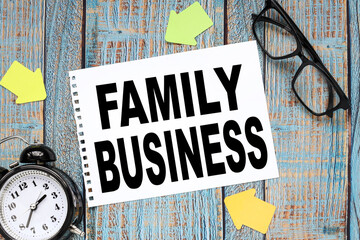 Family Business. on a blue wooden table a sheet of notepad. table clock and glasses in black