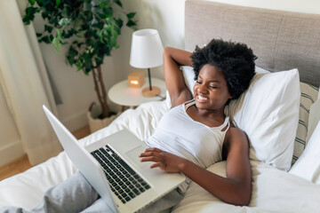 young black woman using a laptop in bright bedroom