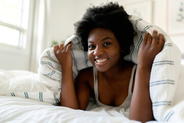 Fototapeta na wymiar beautiful young African woman in tank top lying in bed