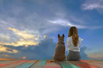 The woman facing the evening sun sits with her pet next to her and enjoys the beauty of nature.