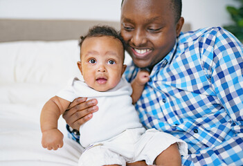 happy young African man playing with his little baby while lying in bed