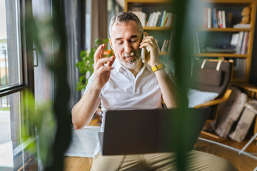 Businessman sitting at desk in bright office, talking on mobile phone
