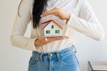Young woman holding small house model in hand, home and insurance protection and control concept.