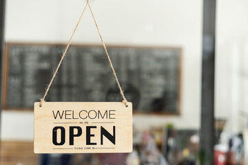 Open a wide sign hanging on the glass door in front of the shop. A business sign stating 'open' in a coffee shop or restaurant hanging at the entrance door. After being closed for a long time because 