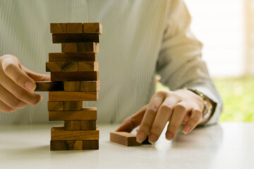 Man hand playing wooden block tower game on white background. Planning, risk and strategy in business. Businessman and engineer pulling wooden blocks on the tower