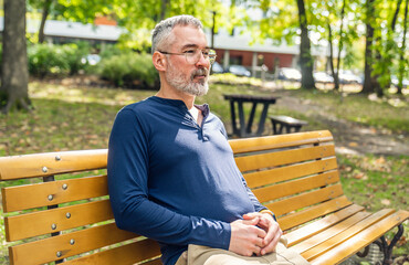 Fototapeta premium Portrait of a mature man sitting on a bench in an urban park