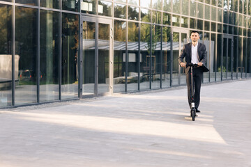 Man rides an electric scooter on the road. Modern way of getting around. Handsome man in a suit riding electric scooter in a city. Adult businessman riding with electric scooter to work