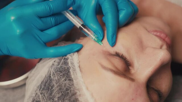 Beauty and injections concept. Experienced beautician entering subcutaneous prick with required active components into female face for tightening and lifting.