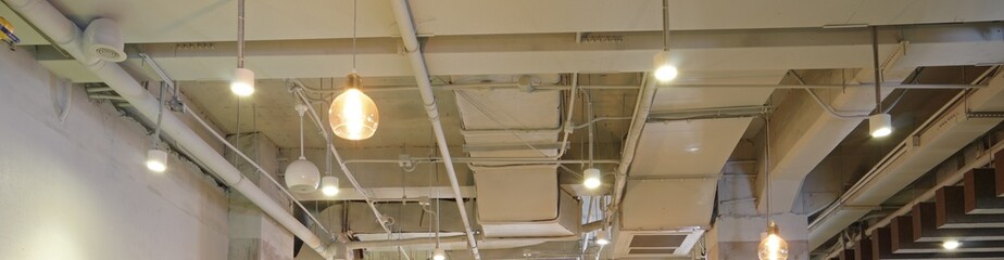 White industrial style ceiling with exposed air conditioner vent grid duct pipes and lamps banner - obrazy, fototapety, plakaty