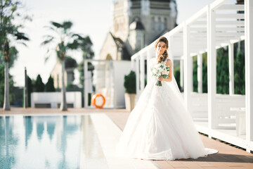 Beautiful bride in elegant white dress holding bouquet posing in park