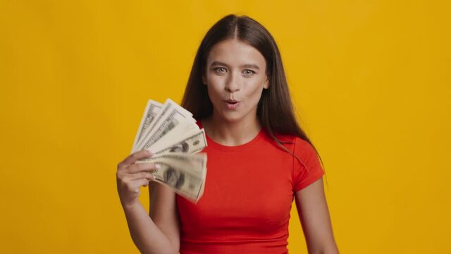 Joyful Woman Holding Money And Throwing Dollar Banknotes, Yellow Background