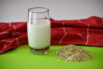 Glass of hemp milk and hemp seeds on a green mat on the table and a red kitchen cloth