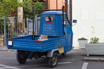 Fototapeta na wymiar A traditional blue three-wheeled vehicle parked on the road (Tuscany, Italy, Europe)